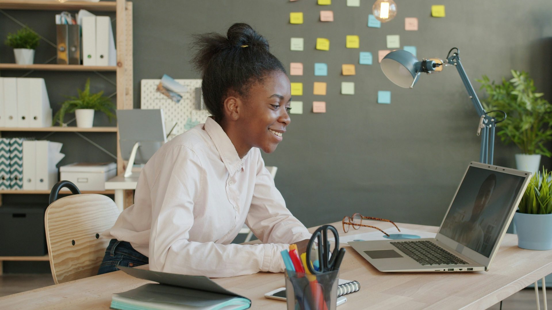 Young woman smiling while working on a laptop at desk.